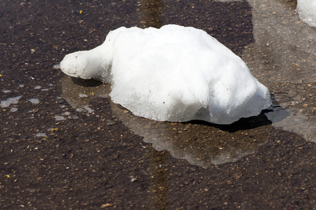 A large pile of dirty white snow lies on the asphalt road (The snow lies in a puddle)の写真素材