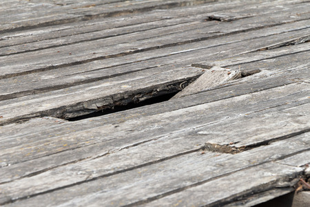 The pit (hole) in the old and worn floor. The material covering the wood. The flooring is gray. Around lie fragments (pieces) of wooden planks.の写真素材