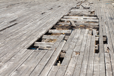 The pit (hole) in the old and worn floor. The material covering the wood. The flooring is gray. Around lie fragments (pieces) of wooden planks.の写真素材