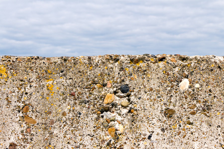 Stone (concrete) fence (block) close-up. Old and not smooth. On the surface growing moss. The background is blurred (sky and clouds).の写真素材