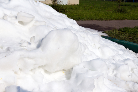 A large pile of dirty and white snow lies on the asphalt road on background green grassの写真素材