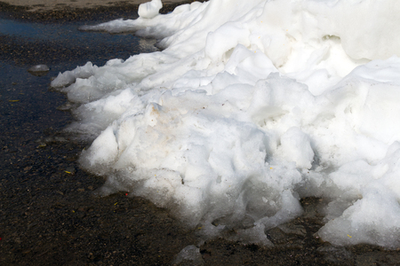 A large pile of dirty white snow lies on the asphalt road (The snow lies in a puddle)の写真素材