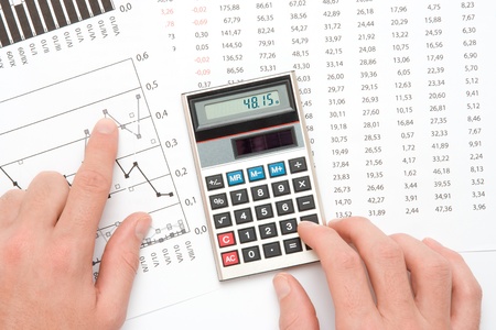 Concept of business analyst - hand with calculating on calculator, sheet and graph from top viewの写真素材