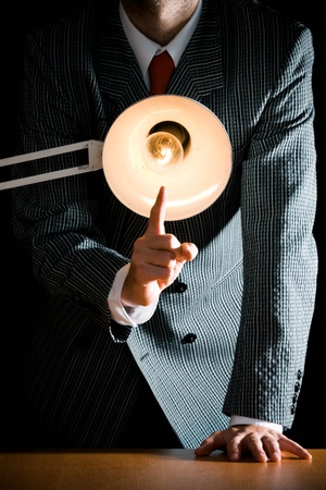 Suggestive interrogation concept - interrogating person standing behind desk lampの写真素材