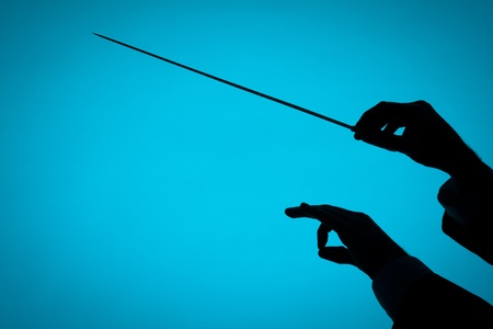 Male orchestra conductor hands, one with baton. Silhouette against blue background.の写真素材