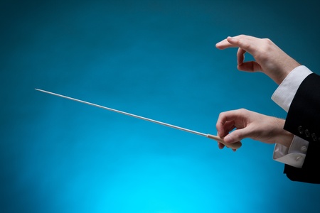 Male orchestra conductor hands, one with baton. Blue background.の写真素材