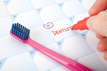 Don't forget visit a dentist concept - man write reminder of dentist in calendar. Selective focused on text dentist.の写真素材