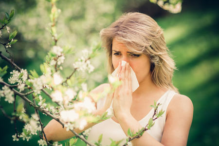 Woman with pollen allergy in springtime near tree in bloom.の写真素材