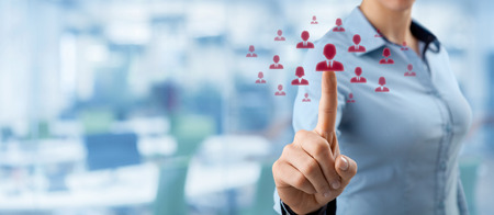 Human resources, CRM and social networking concept - female officer choose person (employee) represented by icon. Out of focused office in background, wide composition.の写真素材