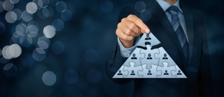 CEO, leadership and corporate hierarchy concept - recruiter complete team represented by puzzle in pyramid scheme by one leader person (CEO). Wide banner composition with bokeh in background.の写真素材