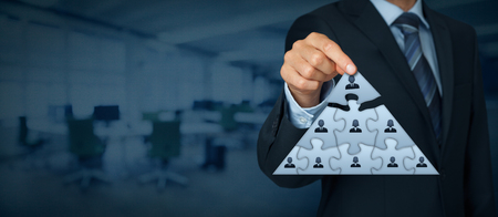 CEO, leadership and corporate hierarchy concept - recruiter complete team represented by puzzle in pyramid scheme by one leader person (CEO). Wide banner composition with office in background.の写真素材