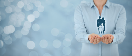 Family life insurance, family services and supporting families concepts. Businesswoman with protective gesture and silhouette representing young family. Wide banner composition and bokeh in background.の写真素材