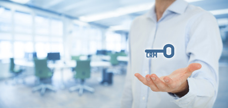 Key to successful CRM concept. Businessman offer Customer Relationship Management solution, represented by key with text CRM, office in background.の写真素材