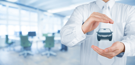 Car (automobile) insurance and collision damage waiver concepts. Businessman with protective gesture and icon of car. Wide banner composition and office in background.の写真素材