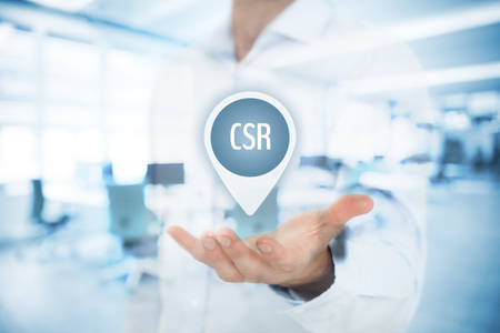 Corporate social responsibility (CSR) concept. Businessman hold virtual label with text CSR,  double exposed with office in background.の写真素材
