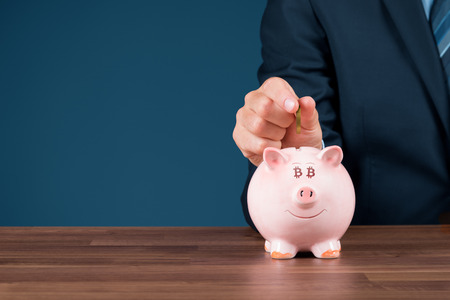 Bitcoin savings and investment concept. Businessman insert bitcoin coin in piggy bank.の写真素材