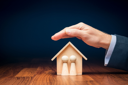 Family life and property insurance concept. Wooden figurines representing family and wooden house and businessman hand with protective gesture, symbol of insurance.の写真素材