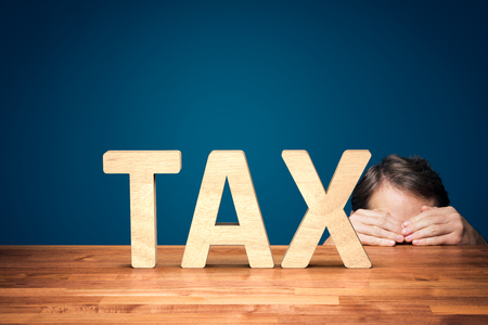 Accountant has a fear of the big tax. Worried or timid businessman is hiding behind the table against big taxes.の写真素材