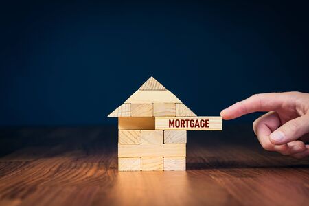 Mortgage concept. Financial agent complete wooden model of the house with last piece with text mortgage.の写真素材
