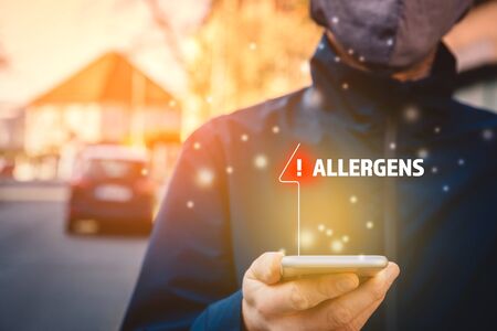 Increased concentration of allergens and polls in the air. Man with mask and smart phone with notification or report about allergens. Modern healthcare concept.の写真素材