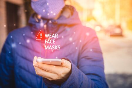 Wear face masks recommendation. Person with smart phone walk on street and look on wear masks notification on his mobile in pandemic times.の写真素材