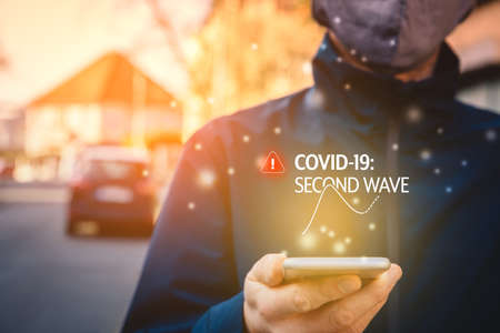 Notification about second wave of covid-19 on smart phone. Concept. Smart phone user read notification outside.の写真素材