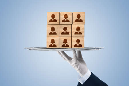 Human resources team on a silver platter - human resources services concept. Hand holding silver platter (salver, tray) and wooden cubes with business person icons.の写真素材