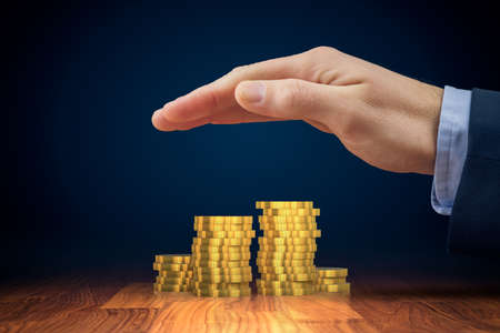 Protect investments and savings, financial insurance concept. Businessman hand with protective gesture and coins of money on table.の写真素材