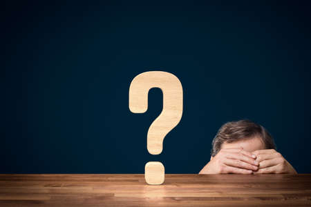 Manager is worried about future and decision making concept. Question mark symbolizing decision making and manager or businessperson hiding behind his hand and the table.の写真素材