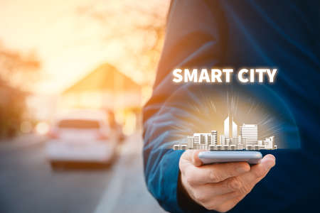 Smart city concept - communication technology (ICT) and Internet of things (IoT) technology integrated to manage city asset. Person with smart phone walk outside on street and symbol of a city.の写真素材