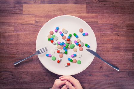 Overuse of drugs, dietary supplements and vitamins concept. Person prepared for eating with cutlery and plate full of drugs and vitamins.の写真素材
