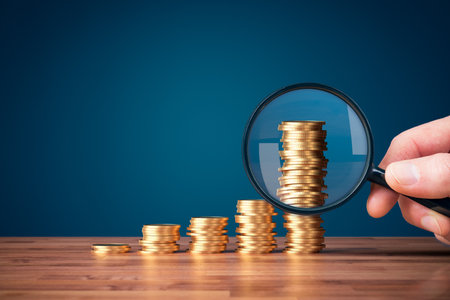 Money makes money investment concept with magnifying glass. Coins in shape of growing graph and focus on the biggest column.の写真素材