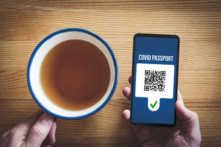 Covid passport certificate (covidpass) concept with smart phone. Person looking on personal covid passport with fictitious QR code on smart phone. Post-covid era concept.の写真素材