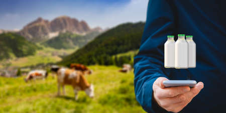 Intelligent agriculture concept with milk production control on smart phone app. Farmer analyze production, cows in background. Customer buy local organic milk directly from farmer.の写真素材