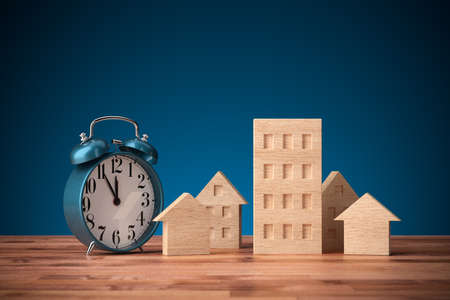 It is five minutes to twelve invest in real estate. Wooden models of different types of houses and alarm clock on five minutes to twelve.の写真素材