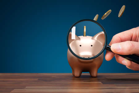 Focus on inflation and reduction of savings concept. Inflation concept with piggy bank, magnifying glass and coins flying away from piggy bank. Tax, charge fee or handling charge concepts.の写真素材