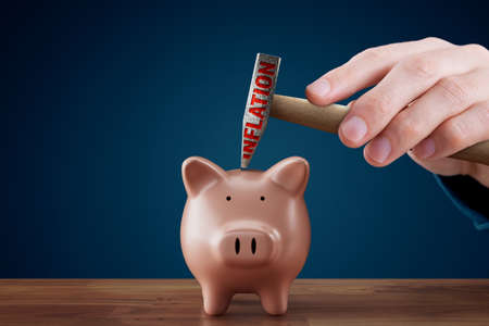 Inflation destroys savings concept. Piggy bank with savings inside, hand with hammer with text inflation, close to destroy piggy bank. Inflation is devaluation of savings.の写真素材
