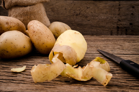 Peel fresh potatoes on rustic wooden background. Raw organic potatoes on old wooden background.の写真素材