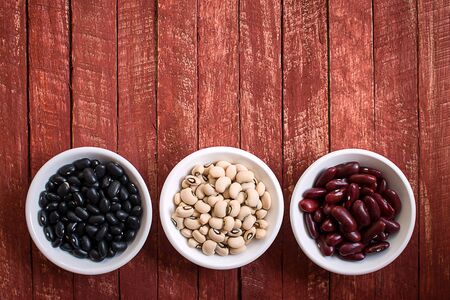Assortment of beans in white bowl on rustic wood. Black beans, Black eyed beans, Red beans on wooden background.の写真素材