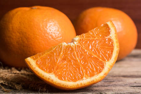 Fresh orange slice and whole orange on wooden table. Oranges are an excellent source of fiber and...