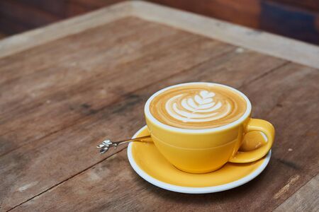 Yellow Cup Of Coffee With Latte Art On Wood Tableの写真素材