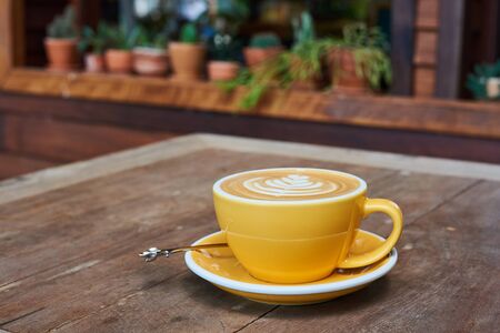 Yellow Cup Of Coffee With Latte Art On Wood Tableの写真素材