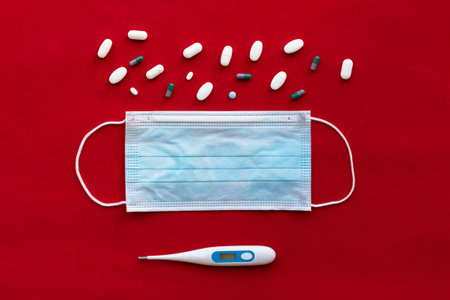 Protective face mask, thermometer and pills on red background. Virus and disease protection concept.の写真素材