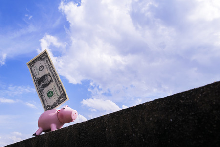 Piggy bank with a dollar plugged in. Walking up steep slopes The backdrop is a bright skyの写真素材