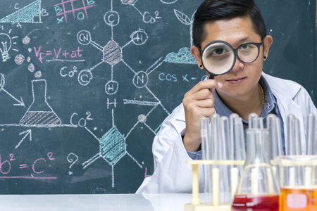 Genetic improvement Scientist with chemicals used in experiments,Backdrop is a chemical formulas writing,Staff with scientific expertise,Wearing a white shirt,Is magnifying glass working.の写真素材