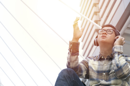 Music is essential to life,Help keep the mind calm,Men are listening to music with headphones,By using the internet signal,Wear a plaid shirt,jeans and glasses.の写真素材