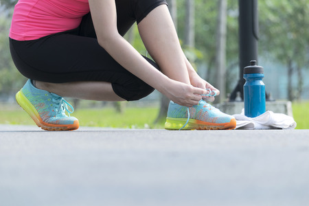 Exercise to keep the body healthy,Women wear pink shirts and black pants are shrunk to tie the shoe,A towel and a water bottle are on the side.の写真素材