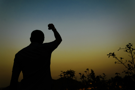 achievement and people concept - silhouette of businessman over sky and sun light background,achievements successful arm up man is on top of hill celebrating success with sunriseの写真素材