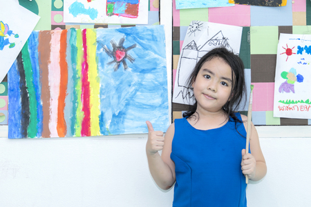 The girl stands in front of his artwork.A thumbs up thumb and 
The other hand holds the paintbrush.の写真素材