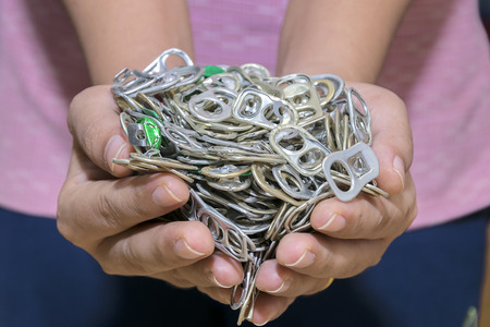 A pile of Aluminum Hand Pull Tab Good Idea for Environmental saving,Donations for Prosthetic leg,Ring pull tab Aluminum Pop Tops of cans in the hands of women.の写真素材